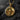 Gold plated variant of winged skull medallion displayed on textured black rock surface