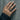 Lifestyle shot of the oxidized silver riveted braided ring worn on an index finger against a textured concrete wall