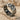 Close-up of oxidized silver Cuban chain ring resting on sand with small seashells highlighting the rustic finish.