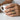 Ascending Koi Wave Ring, two-tone finish, worn on model hand holding a cup