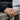 Man wearing gold Navy signet ring on finger outdoors while resting hand on a wooden pier near water