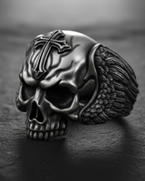 Close-up 3/4 view of a handcrafted silver skull cross ring, showing the oxidized finish and intricate feather details on the wings.
