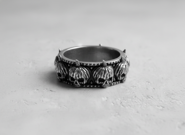 Silver pumpkin skull ring featuring row of jack-o-lanterns with stems on grey textured surface