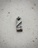Front view of rectangular silver pendant showing deep grooves and weathered surface details on light background
