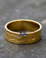 Yellow gold textured ring variant with raw blue sapphires embedded in crack design on grey stone background