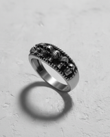 Angled shot of gothic silver ring casting shadow showing repeating skull motif and beaded rim texture