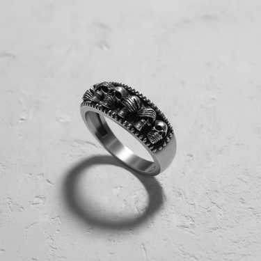 Angled shot of gothic silver ring casting shadow showing repeating skull motif and beaded rim texture