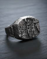 Close-up of textured silver rock signet ring face mimicking rough weathered earth surface