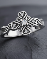 Close-up of silver cross ring showing four-pointed knot design with sparkling gemstone accents and oxidized finish