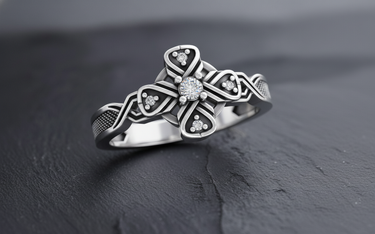 Close-up of silver cross ring showing four-pointed knot design with sparkling gemstone accents and oxidized finish