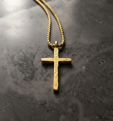Gold plated silver cross necklace with rugged surface design lying on textured slate background