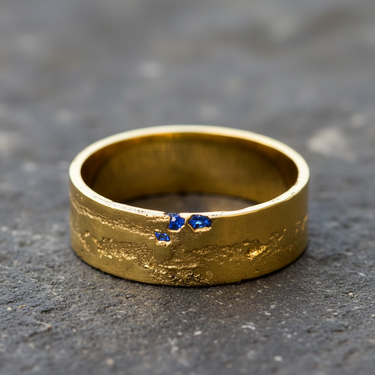 Silver raw texture ring in gold vermeil with blue embedded stones on grey stone background