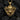 Front view of gold gorilla pendant with baroque leaf details and stern expression placed on dark textured coal.