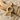 Close-up of gold vermeil bird letter R pendant resting on textured driftwood and soft white beach sand