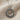 Close-up of handcrafted Anatolian sun disk pendant resting on textured beige linen showing oxidized details