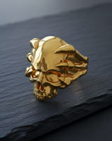 Golden variant of the skull clutch ring showcasing the detailed jaw and claw design on a dark slate surface