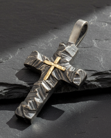 Angled view of handcrafted silver rustic cross pendant with gold vermeil center on dark slate background