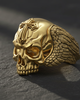 A 3/4 view of the skull cross ring design in a polished gold finish, highlighting the menacing expression and winged band.