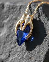 Gold vermeil silver gothic hands pendant holding blue teardrop gemstone on dark stone background