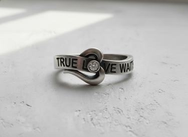 Front view of silver true love waits ring featuring wrap around heart design and center stone on textured background