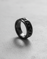 Black rhodium plated 925 sterling silver chain spinner ring standing upright on textured grey background