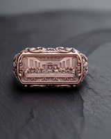 Rose gold tone religious ring with ornate scrollwork on the sides and The Last Supper scene engraved on the bezel