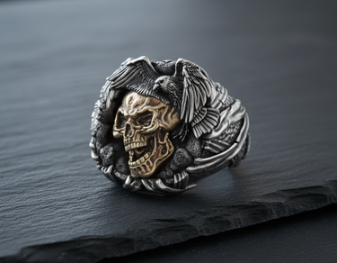 Front view of handcrafted silver raven skull ring featuring a golden skull and detailed silver bird wings on dark background