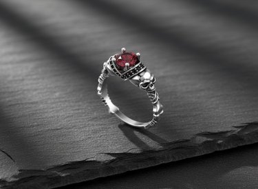 Detailed side view of silver gothic ring showing realistic skull motifs and crown setting with black stone accents