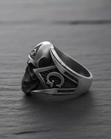 Side profile of silver freemason ring displaying intricate gothic skull details and masonic emblems on dark stone background