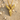 Close-up of the intricately carved gold vermeil bird Y pendant resting gracefully on textured natural beach sand