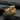 Close-up of gold embracing figures ring resting on dark textured stone highlighting the sculptural craftsmanship