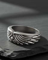 Side profile of handcrafted silver plumage ring highlighting band thickness and comfortable fit on stone surface