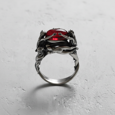Front view of 925 sterling silver ring with three graces design holding a red cabochon stone on grey background