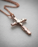 Rose gold plated silver hammered cross pendant hanging on chain against soft grey background