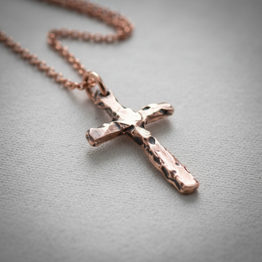 Rose gold plated silver hammered cross pendant hanging on chain against soft grey background