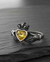 Oxidized sterling silver Claddagh ring showcasing the contrast between the polished band and the detailed hands holding a yellow gem.