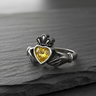 Oxidized sterling silver Claddagh ring showcasing the contrast between the polished band and the detailed hands holding a yellow gem.