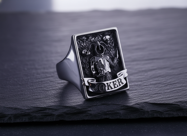 Front view of silver Joker signet ring featuring jester holding a skull with gothic banner detail on dark stone background