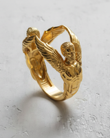 Gold vermeil angel ring sculpture featuring two winged figures on textured white background
