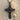 Close up of handcrafted gothic cross pendant resting on textured sand next to a small shell highlighting silver details.