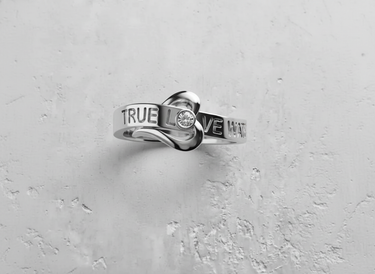 Detailed close up of silver promise ring with heart shape and sparkling stone setting on light grey surface