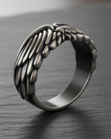 Close-up of handcrafted silver feather ring design with smooth inner band and matte finish styling on textured surface