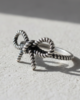 Handcrafted 925 sterling silver bow knot ring with twisted rope texture displayed on a neutral stone surface