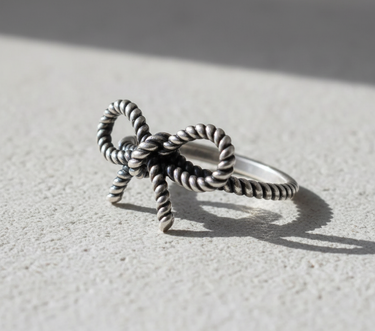 Handcrafted 925 sterling silver bow knot ring with twisted rope texture displayed on a neutral stone surface