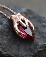 Rose gold plated silver hands garnet pendant holding pear shaped red stone on dark texture background