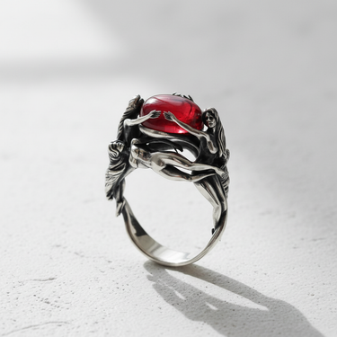 Angled close-up of art nouveau style silver ring with mythological figures and red stone