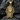 Close-up of golden pharaoh pendant with detailed black stones resting on dark textured slate background