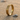 Close-up of the gold vermeil Celtic knot ring standing upright on textured beach sand next to a small seashell at sunset