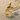 Radiant 14K gold vermeil initial bird letter C pendant resting on textured sand next to a delicate seashell