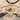 Close-up of gold infinity cross pendant with blue gems resting on light sand and rustic wooden driftwood